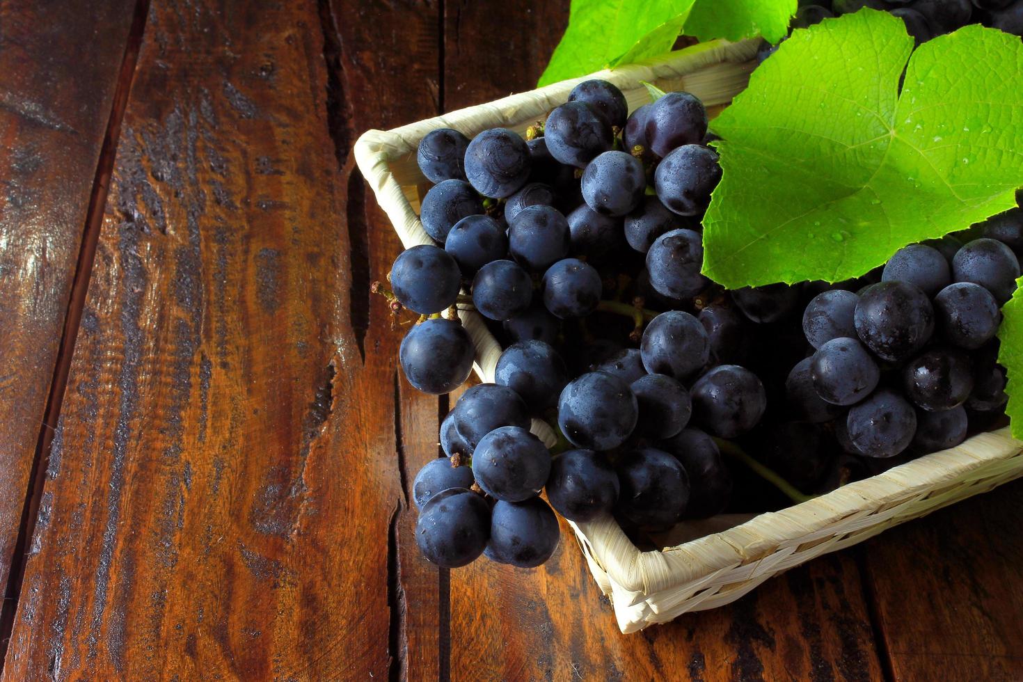 Racimos de uvas, dentro de la cesta de fibra de bambú sobre mesa de madera foto