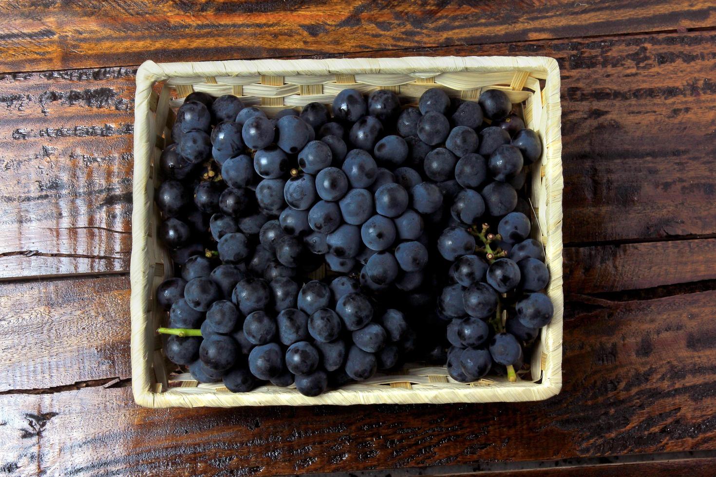 Racimos de uvas, dentro de la cesta de fibra de bambú sobre mesa de madera foto