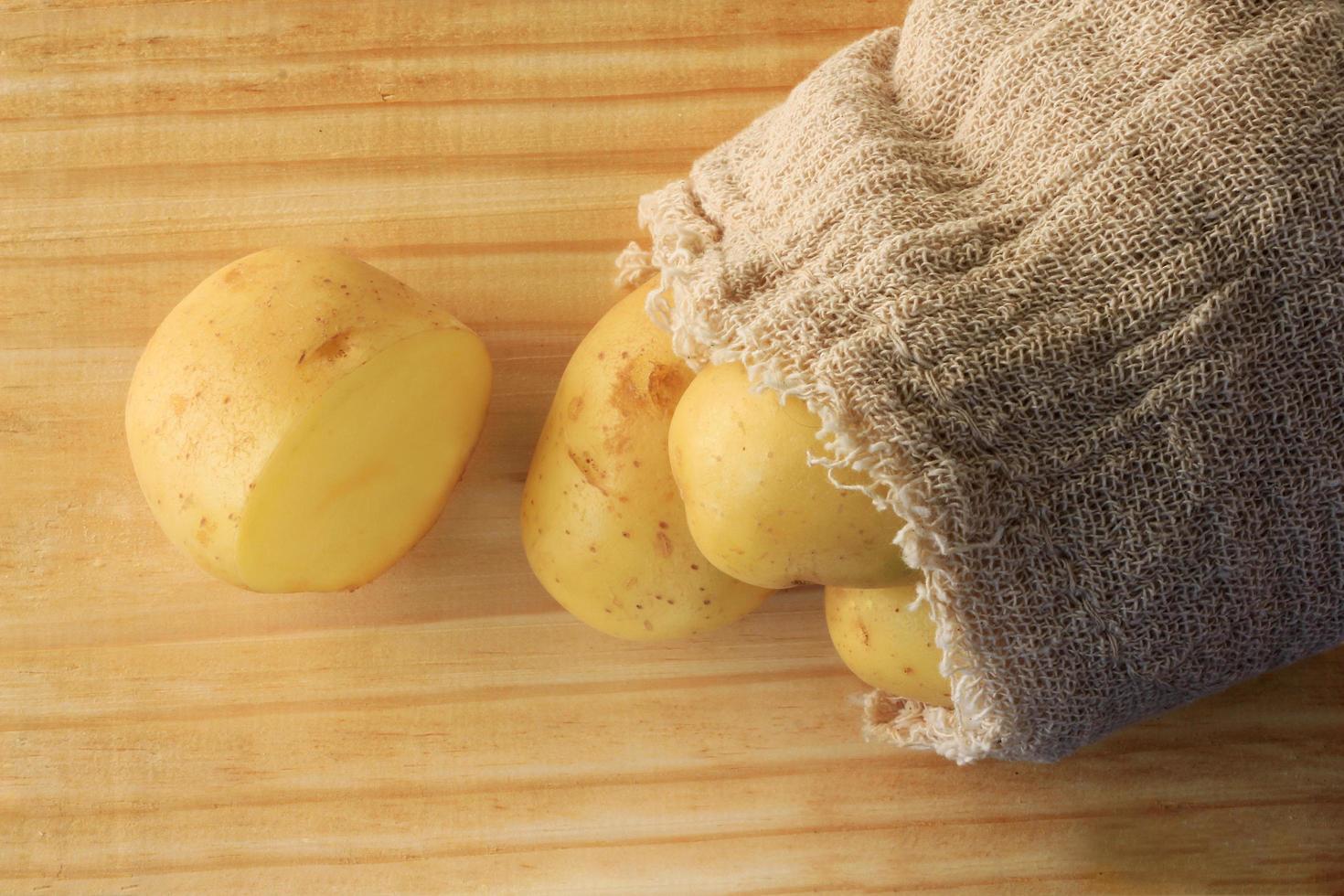 potato sticking out of sack on wooden table, cut potato photo
