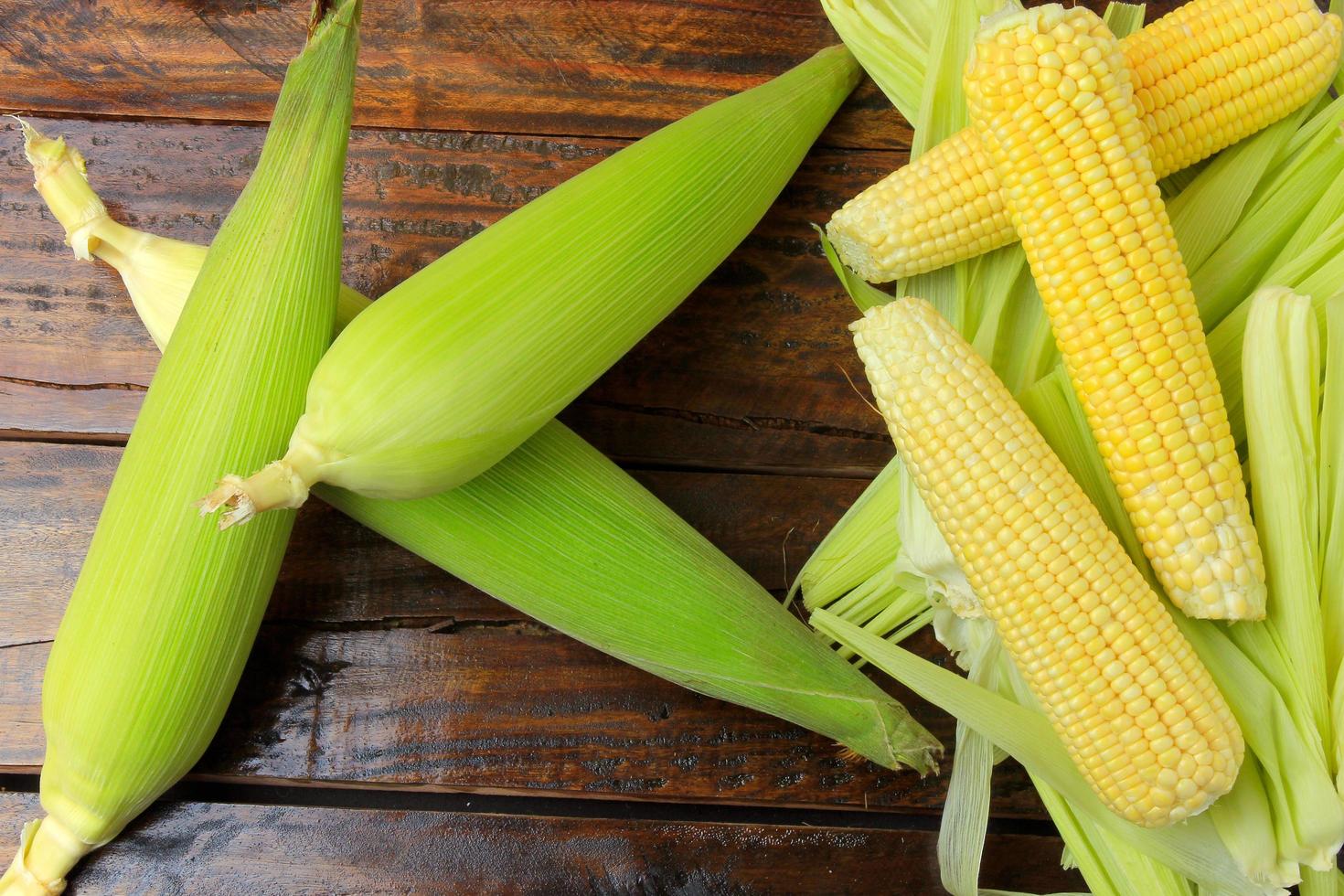 ear of raw corn, with straw and bark, harvested from plantation, on rustic wooden table. photo