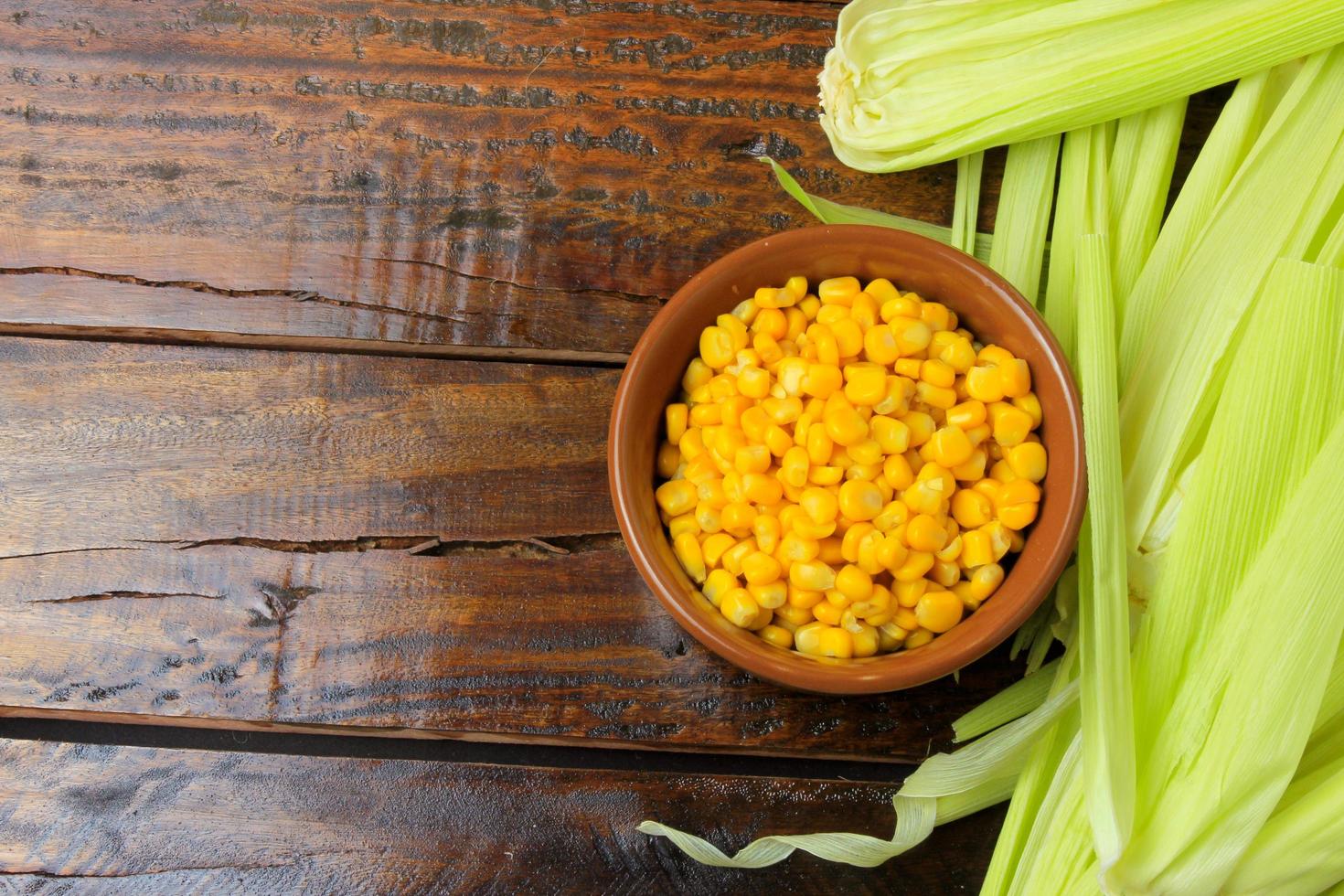 Raw corn kernels, inside ceramic bowl, next to corn on the cob on rustic wooden table. photo