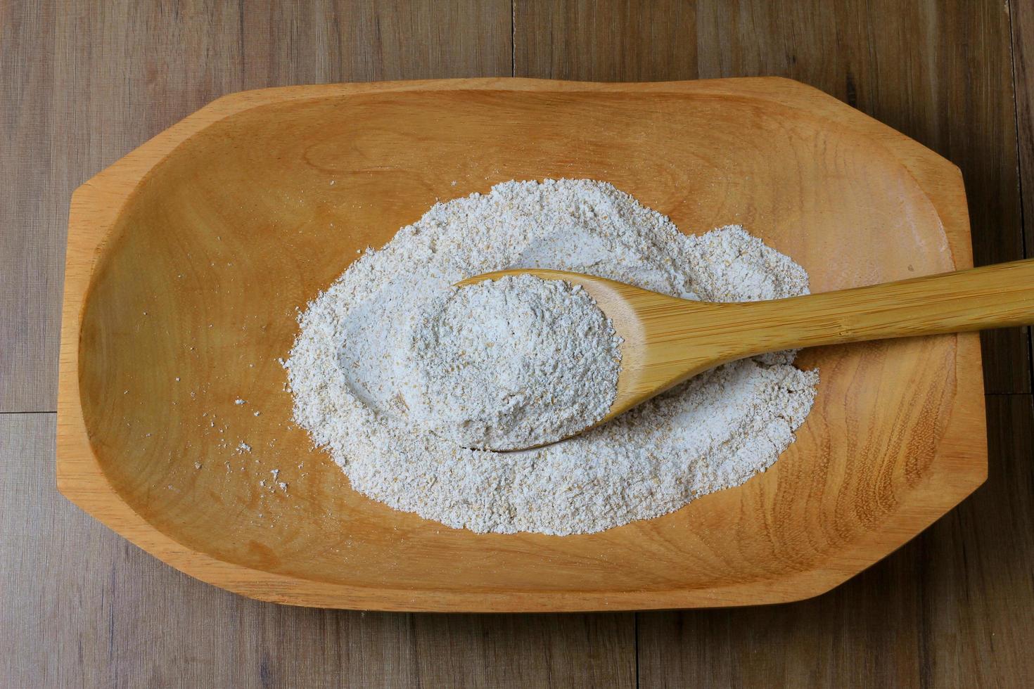 portion of raw whole wheat flour, wooden bowl, wooden table top view photo