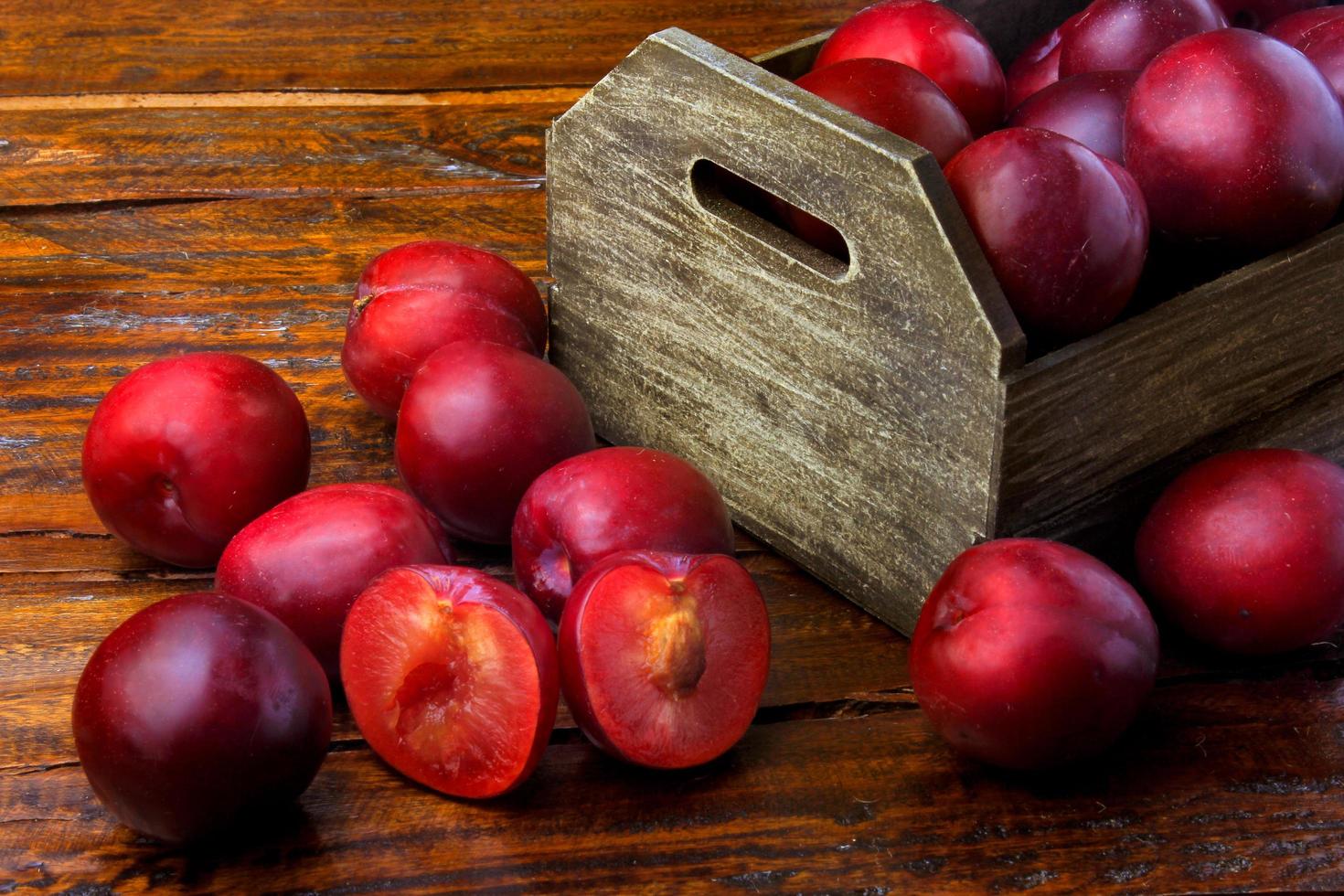 raw and fresh organic plums inside rustic fabric wooden box on rustic table photo