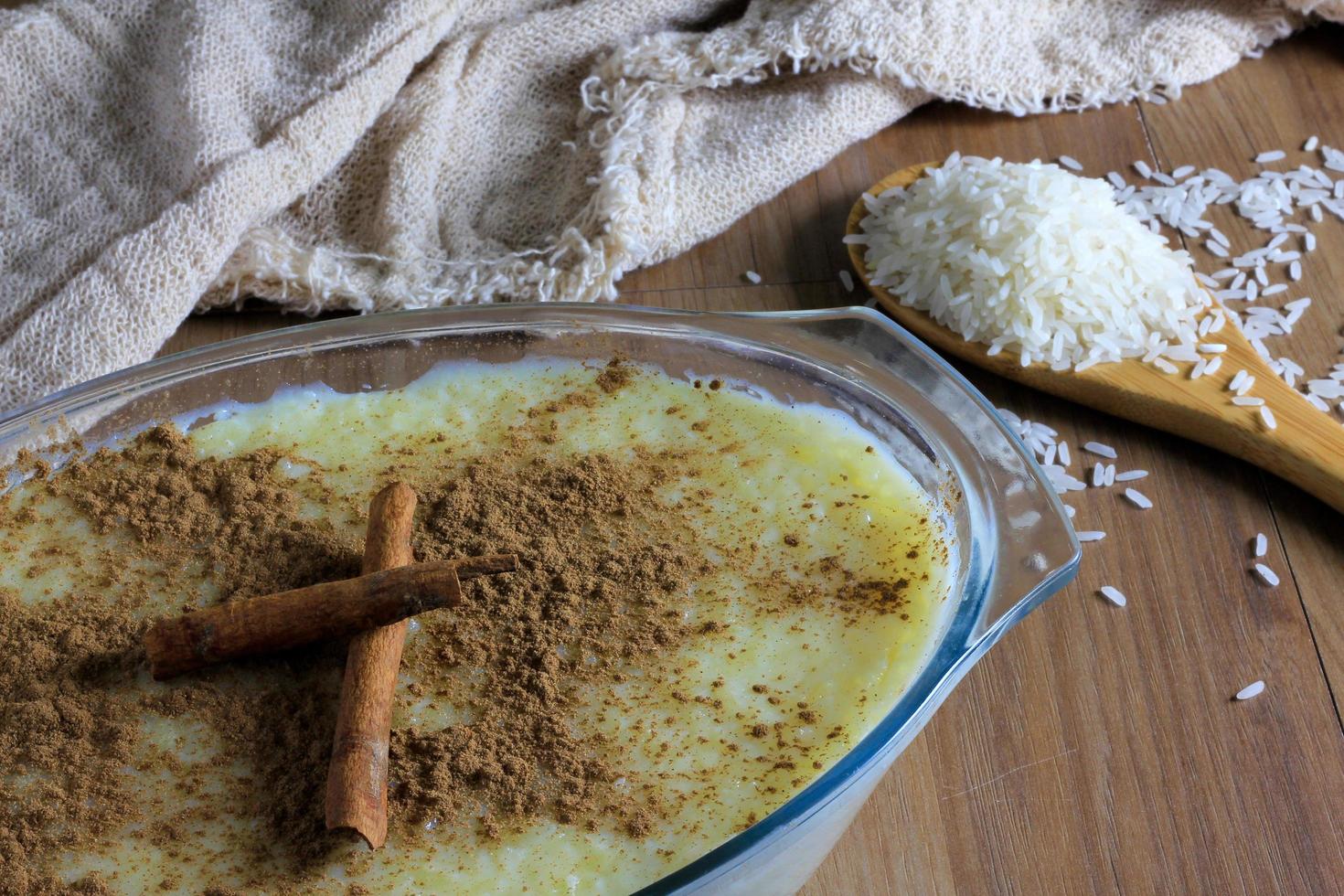 close up rice pudding with cinnamon in glass container, wooden spoon with raw rice photo