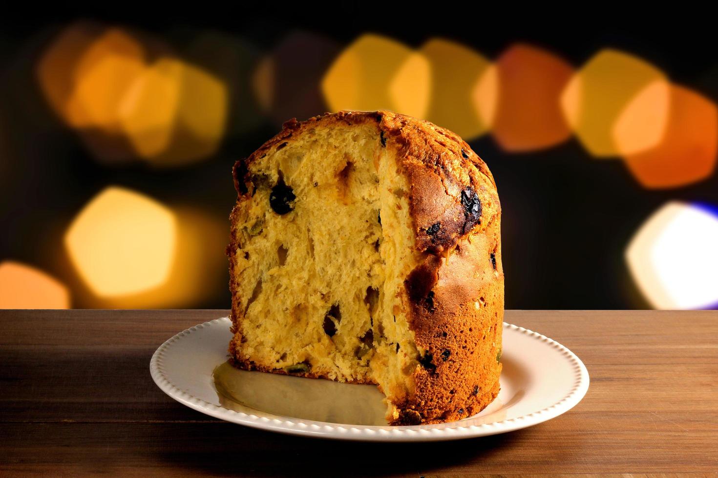 closeup panettone inside ceramic dish on wooden table, bokeh background with lights photo