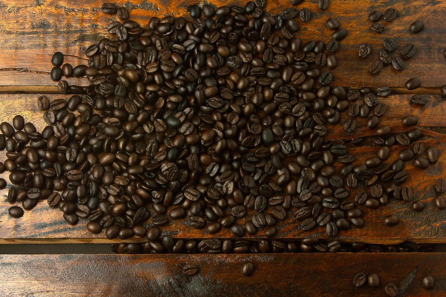 Granos de café tostados esparcidos sobre una mesa de madera rústica. vista superior foto
