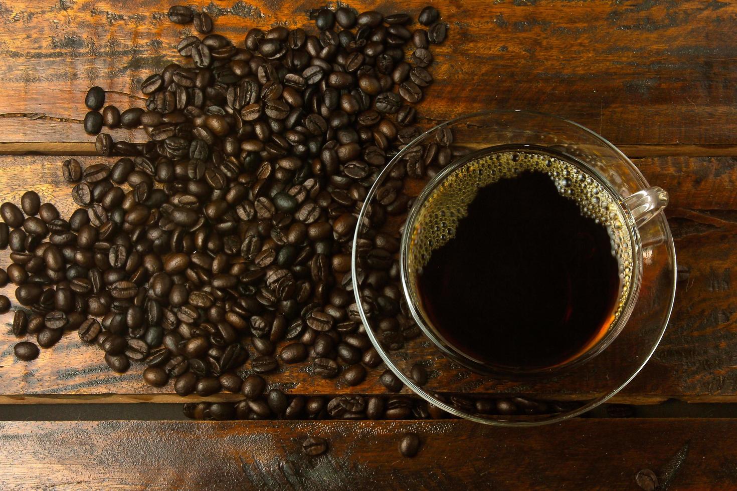 Taza con café recién hecho y granos tostados derramados sobre la mesa de madera rústica foto