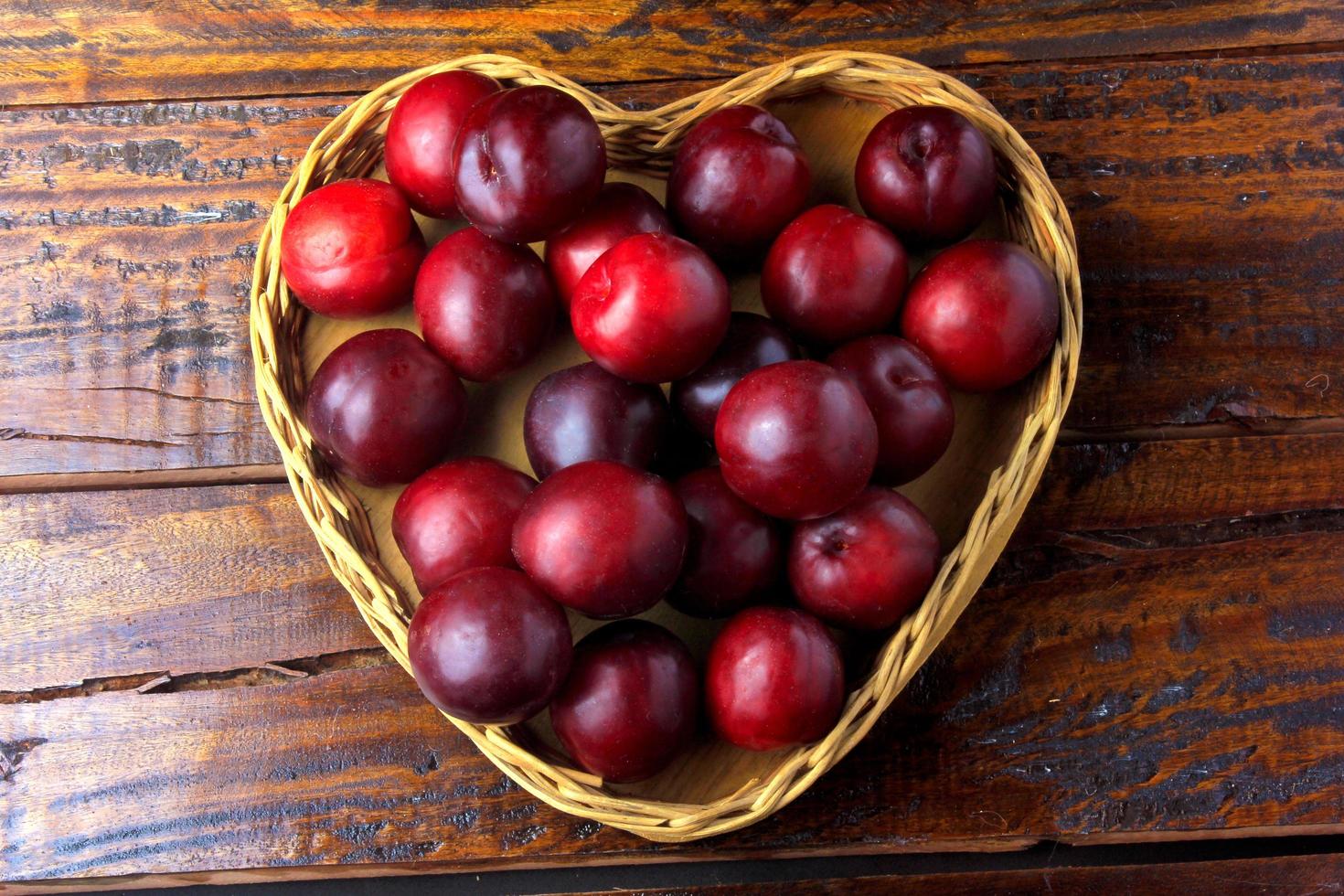 raw and fresh organic plums inside basket with heart shape on rustic wooden table photo