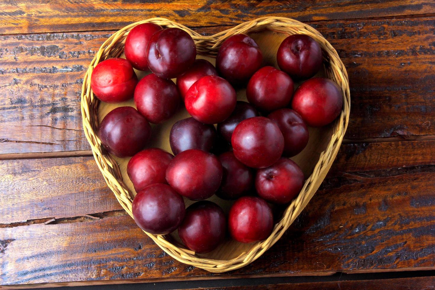 Ciruelas orgánicas crudas y frescas dentro de la canasta con forma de corazón sobre la mesa de madera rústica foto