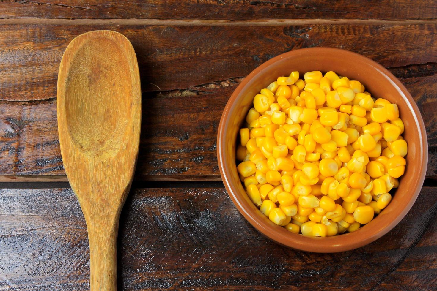 Raw corn kernels, inside ceramic bowl, next to wooden spoon on rustic wooden table. space for text photo