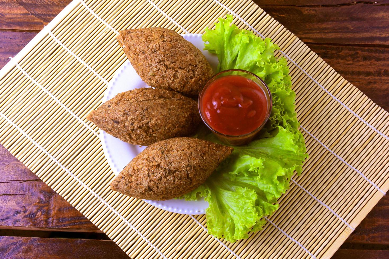 Fried kibbeh with tomato sauce on a plate, over rustic wooden table photo