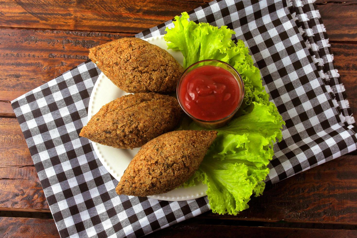 Kibbeh frito con salsa de tomate en un plato, sobre una mesa de madera rústica foto