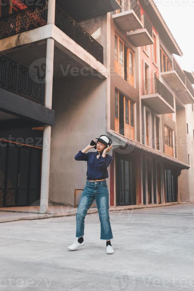 Feliz joven mujer asiática escuchando música y divirtiéndose con auriculares a través de un teléfono inteligente en la calle foto