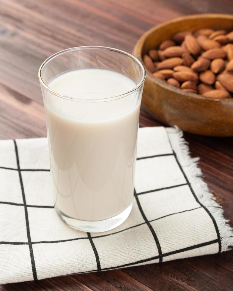 Leche de almendras en el vaso con almendras en un tazón de madera sobre la mesa, merienda saludable, comida vegetariana foto