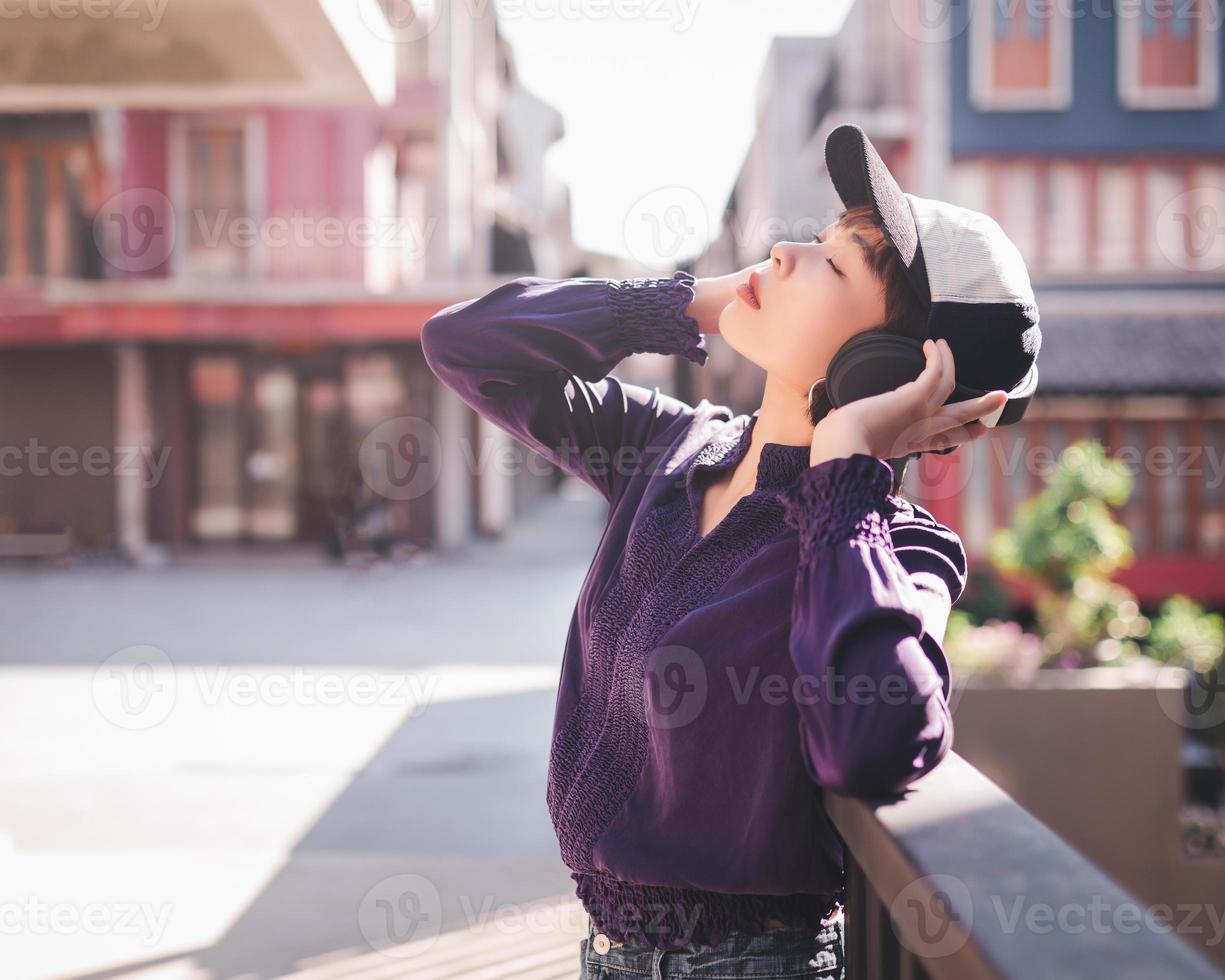 Feliz joven mujer asiática escuchando música con auriculares en la calle foto