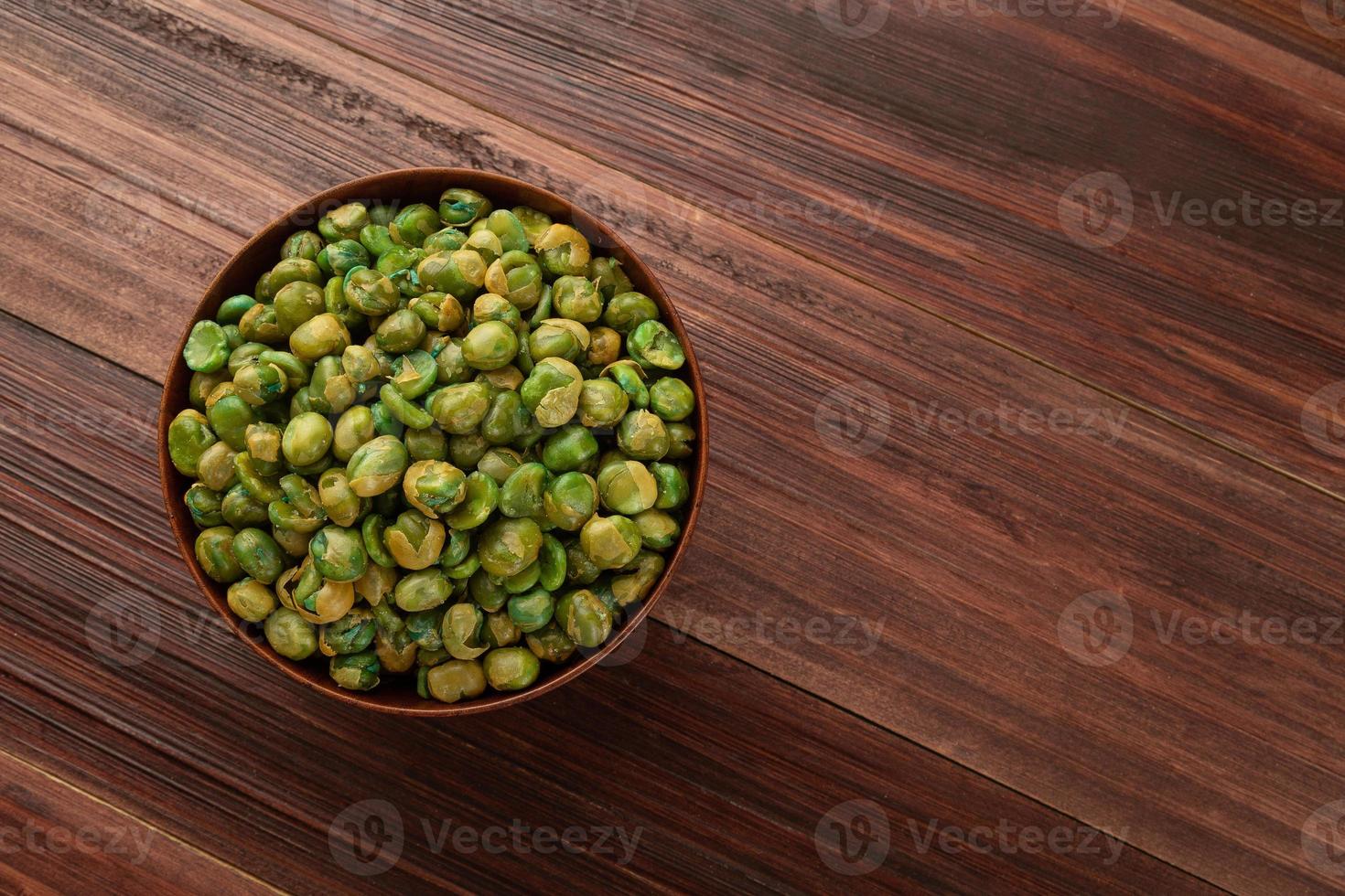 Guisantes salados en un tazón de madera sobre la mesa, merienda saludable, comida vegetariana foto