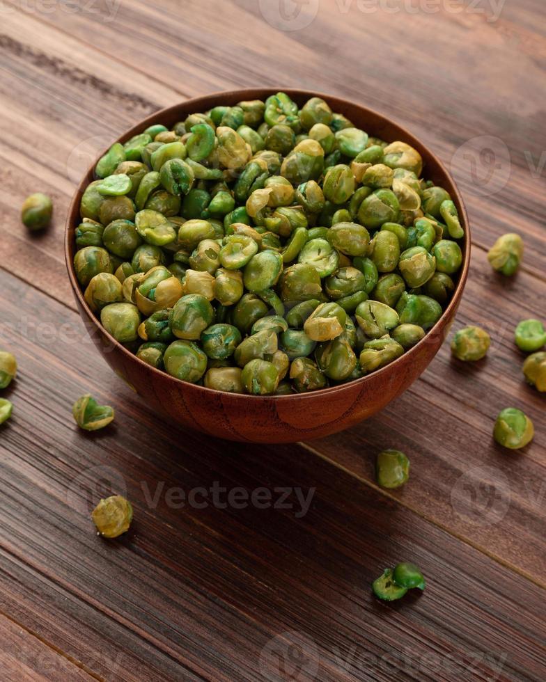 Guisantes salados en un tazón de madera sobre la mesa, merienda saludable, comida vegetariana foto