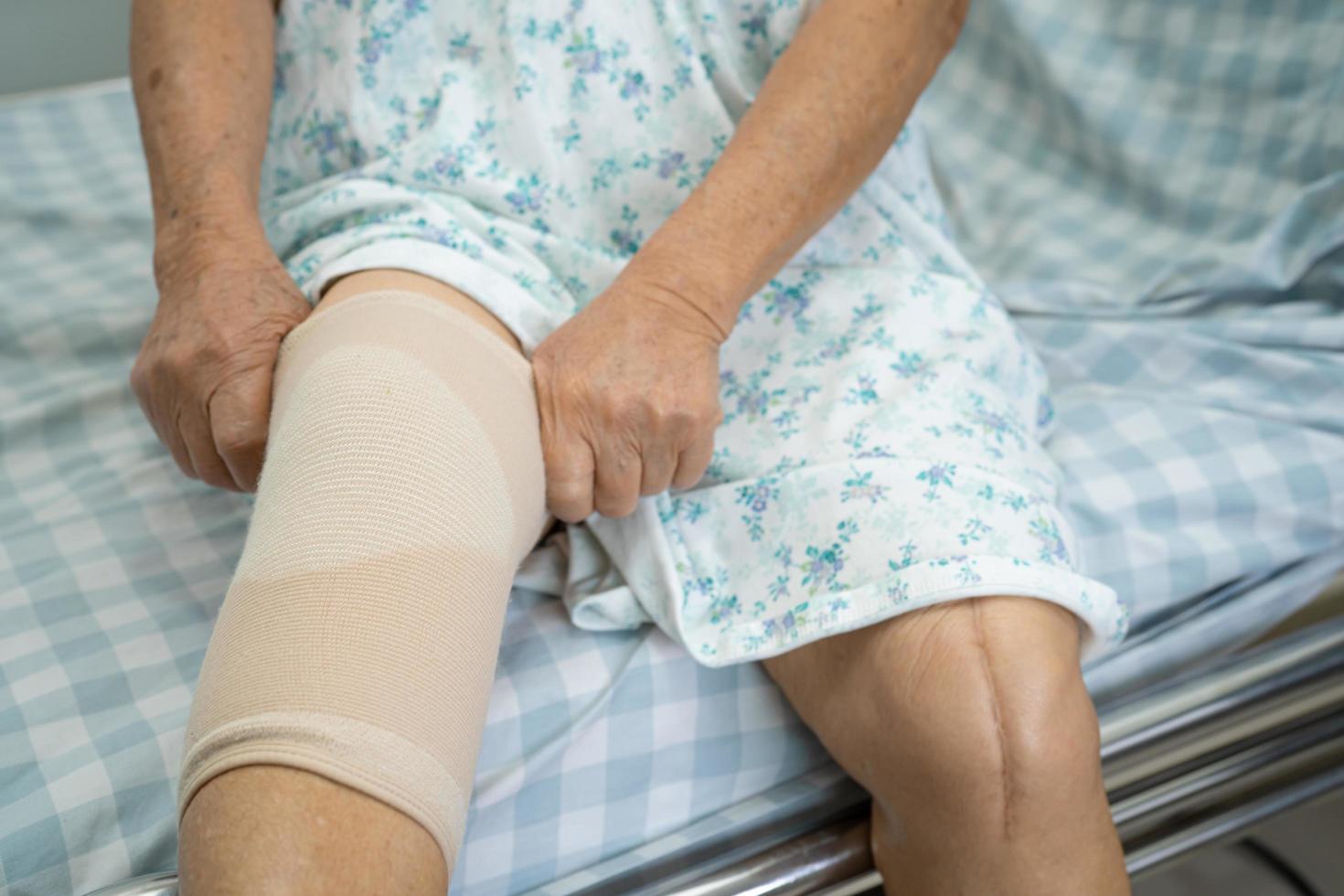 Asian senior or elderly old lady woman patient with knee support pain joint on bed in nursing hospital ward, healthy strong medical concept. photo