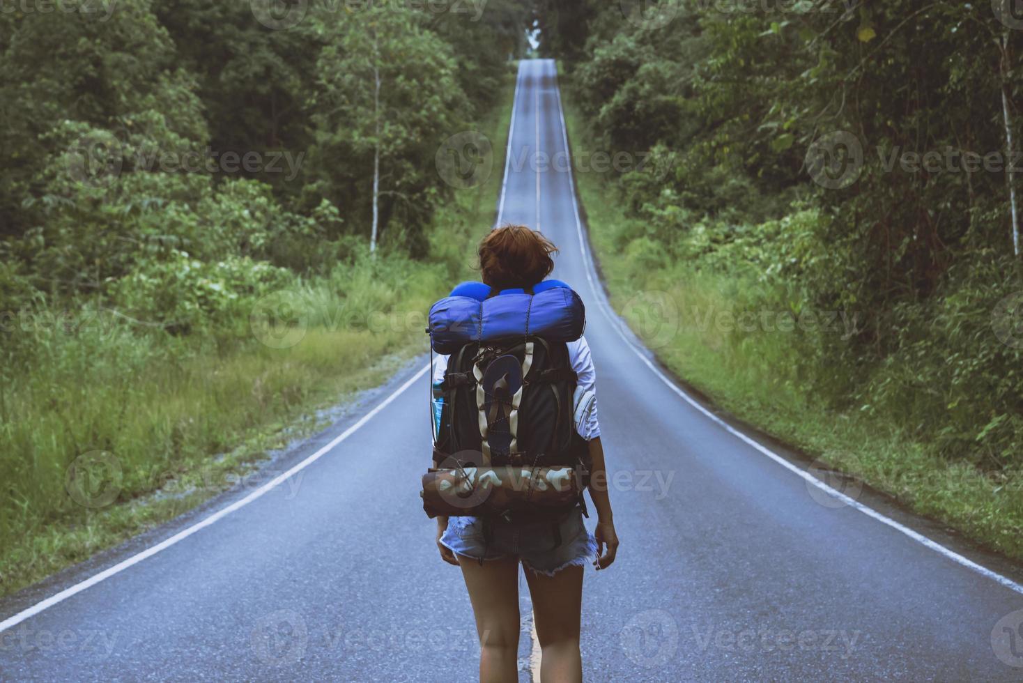 mujer viajero de la libertad de pie con los brazos levantados y disfrutando de una hermosa naturaleza en un camino rural. mujer con mochila de viaje en el campo en una montaña. foto