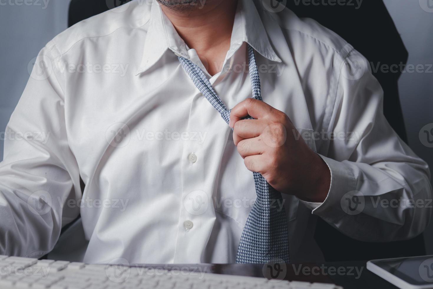Close up portrait of exhausted frustrated stressed handsome sad unhappy upset entrepreneur trying to take off uncomfortable tie formal wear isolated at office., tired businessman taking off necktie. photo