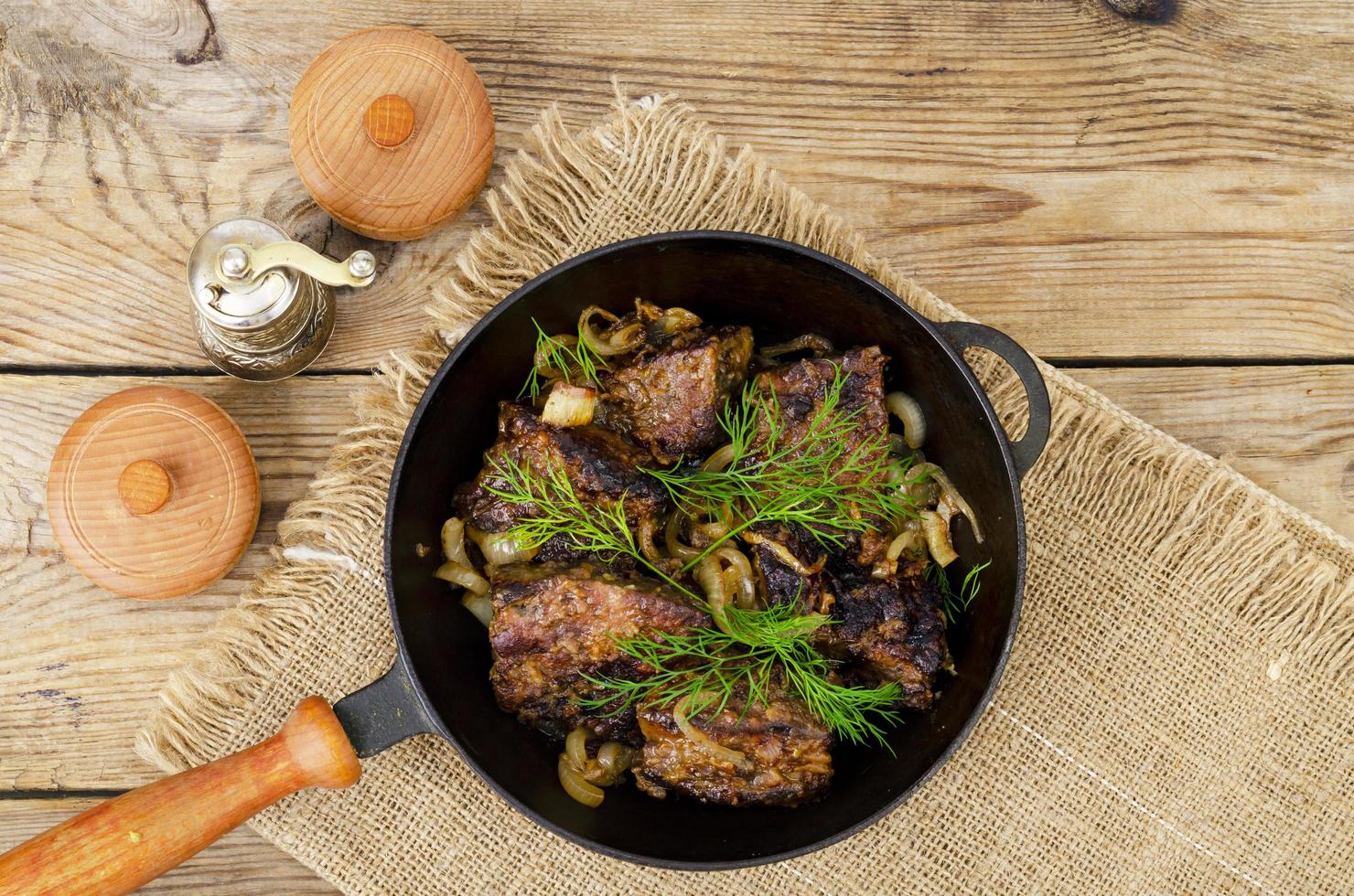 Cast-iron frying pan on wooden table with fried liver. photo