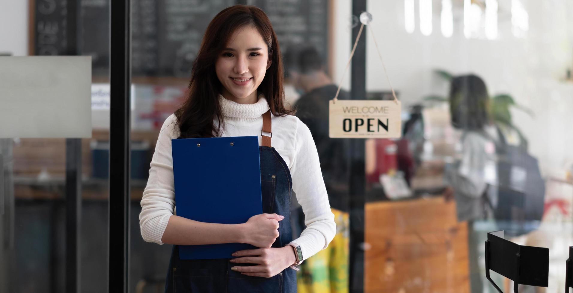 retrato de una hermosa mujer asiática en un delantal de pie en una cafetería, ella es propietaria de una cafetería, el concepto de un negocio de alimentos y bebidas. gestión de la tienda por una mujer de negocios. foto