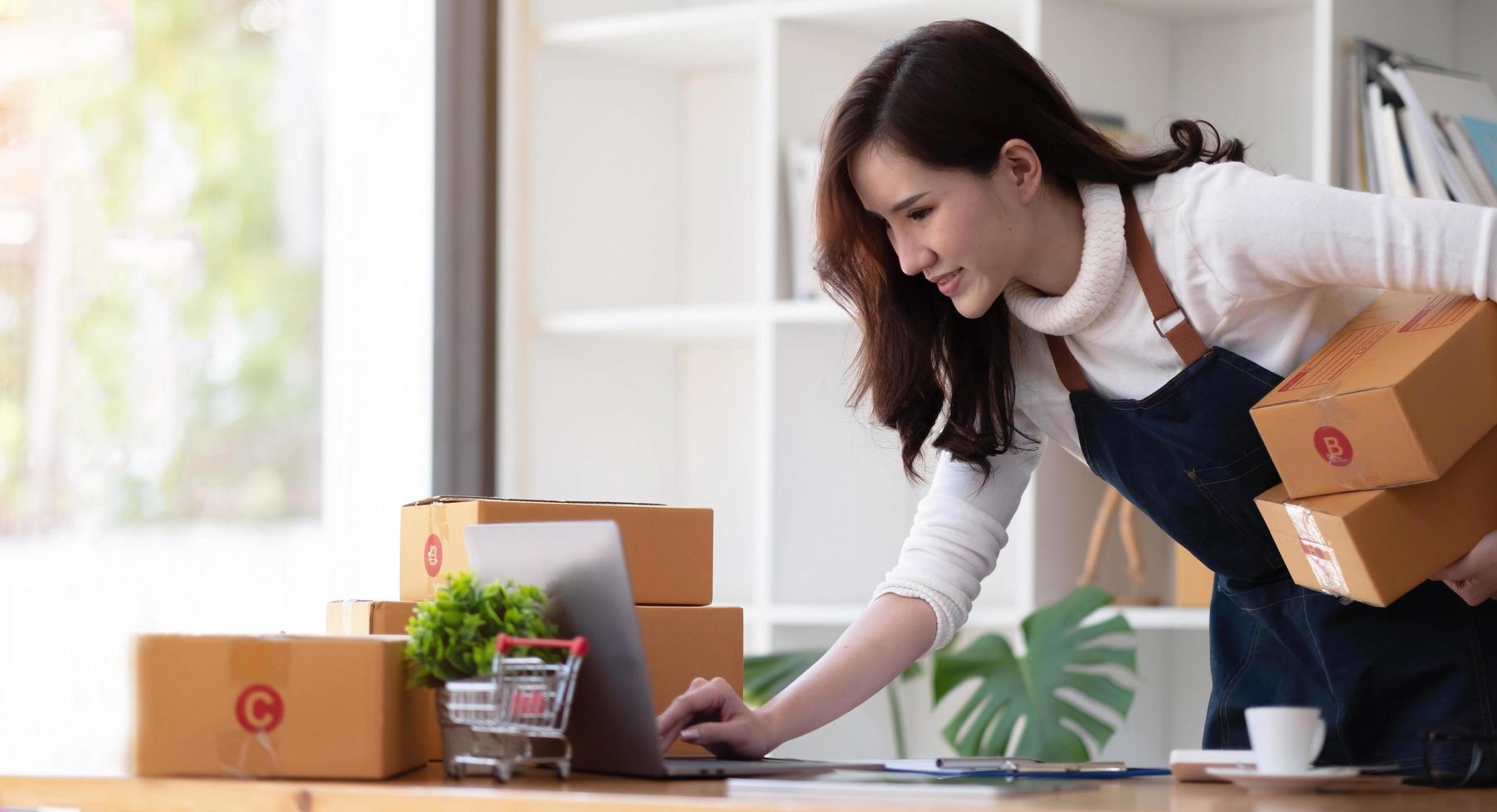 emprendedor de pequeñas empresas, autónomo, retrato de mujer joven que trabaja en la oficina en casa, caja, teléfono inteligente, computadora portátil, en línea, marketing, empaque, entrega, pyme, concepto de comercio electrónico foto