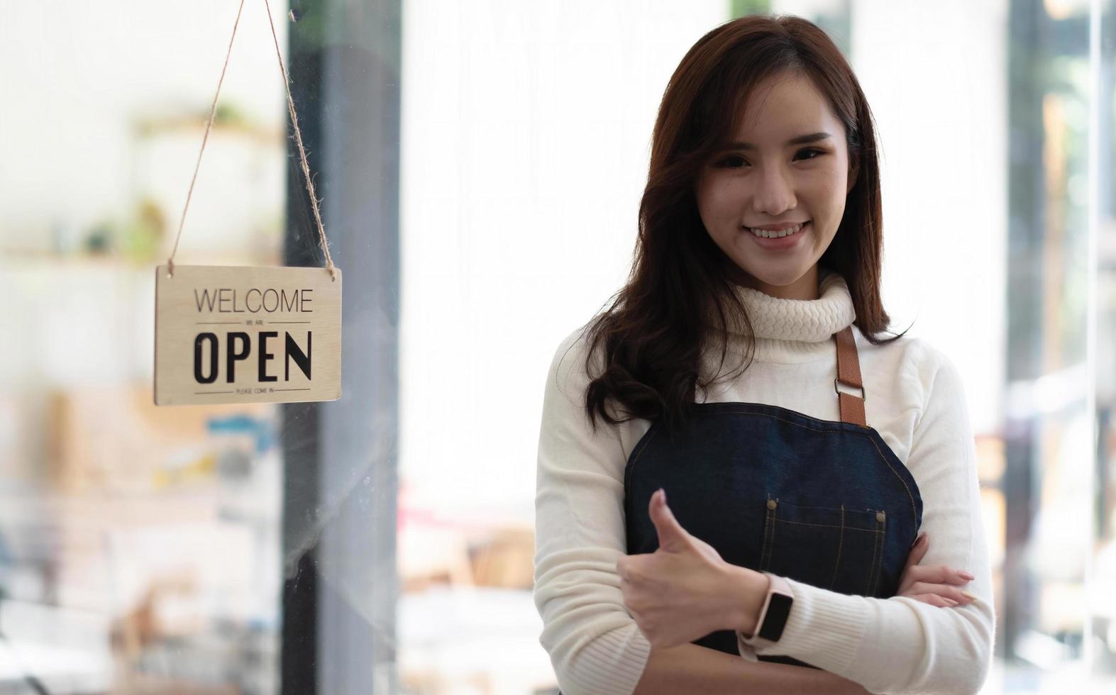 Successful small business owner standing with crossed arms with employee in background preparing coffee photo