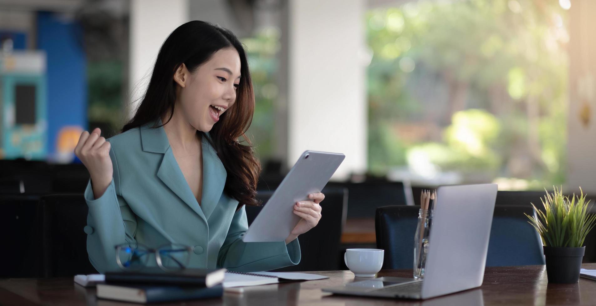 La mujer de negocios asiática está encantada y feliz con el trabajo que hacen en su computadora portátil y tomando notas en la oficina. foto