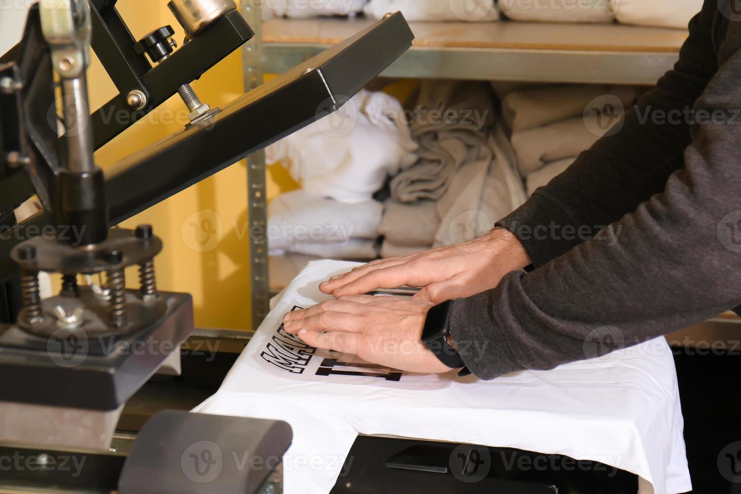 Young man printing on t-shirt at workshop photo