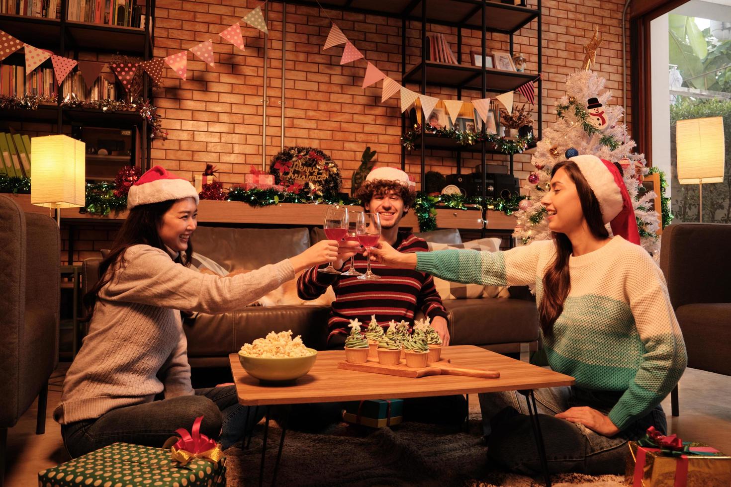 felicidad, la familia y los amigos están celebrando, levantando copas y una sonrisa alegre con bebidas, cupcakes y palomitas de maíz en la sala de estar de la casa, decorada para la fiesta de Navidad y el día de año nuevo. foto