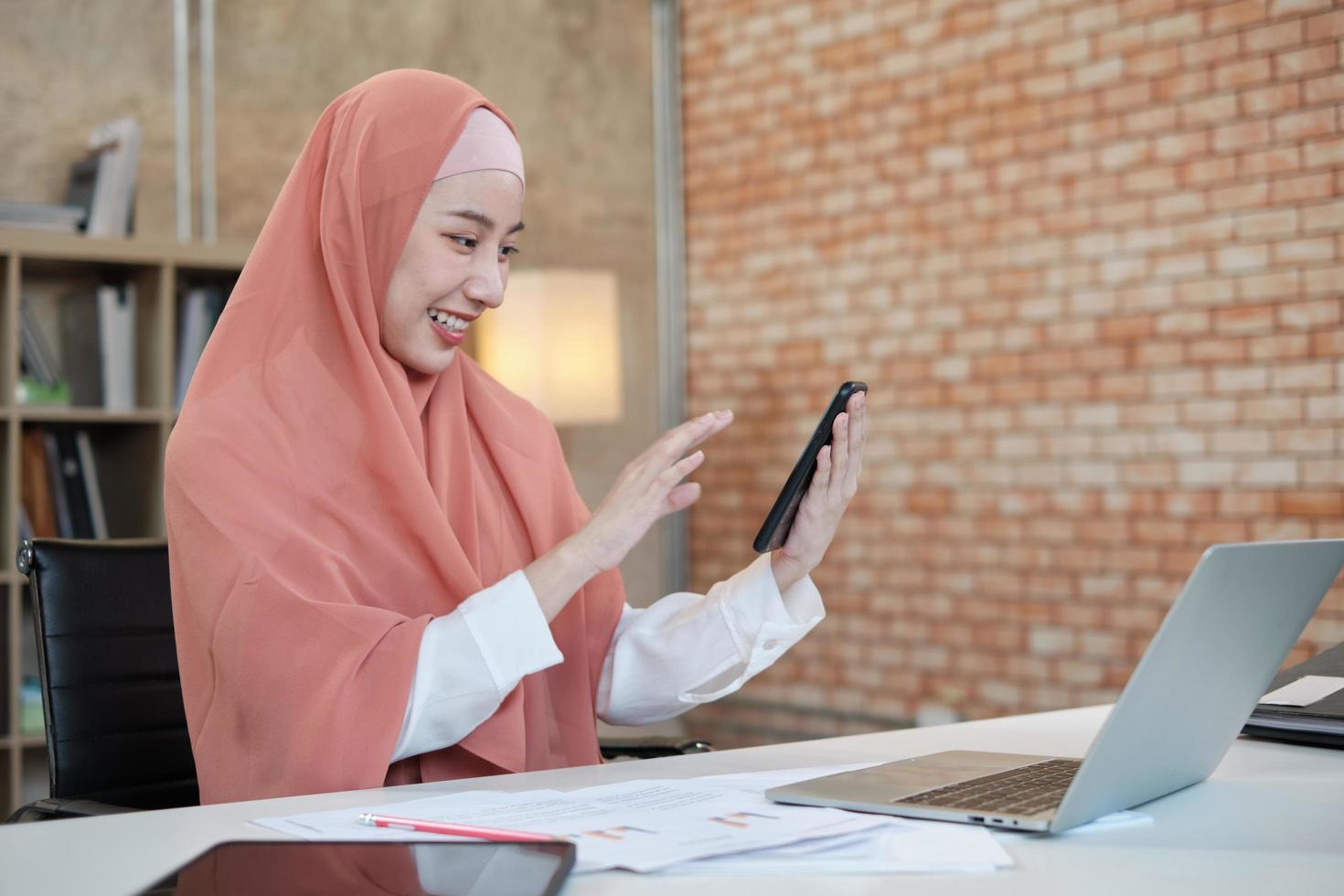 Beautiful businesswoman who Islamic female person is talking on her mobile phone communication and happy smiling because internet online order in laptop, modern lifestyle, e-commerce occupation. photo