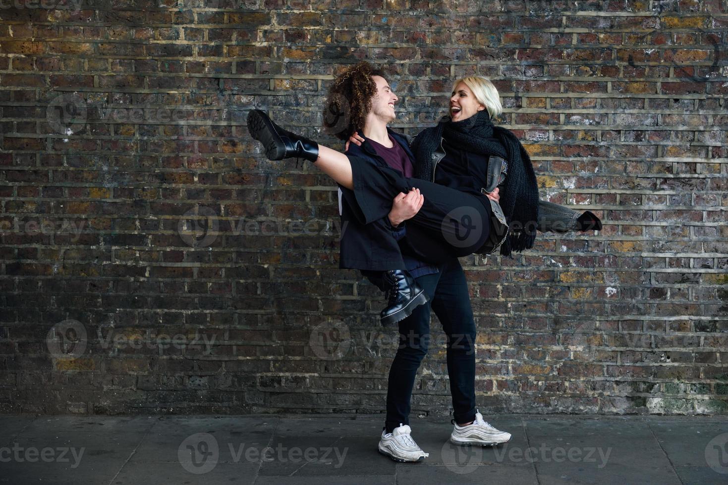 Man holding his girlfriend in his arms in front of a brick wall typical of London photo