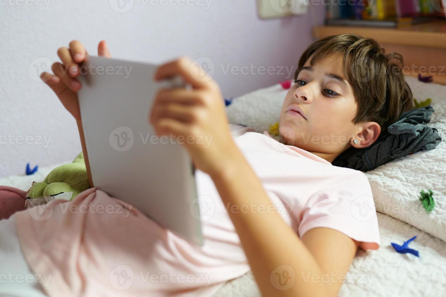 Cute girl using a tablet computer in her bedroom photo