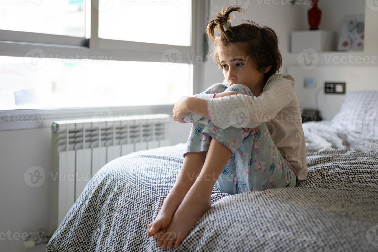 Niña de nueve años sentada en la cama aburrida por el encierro foto