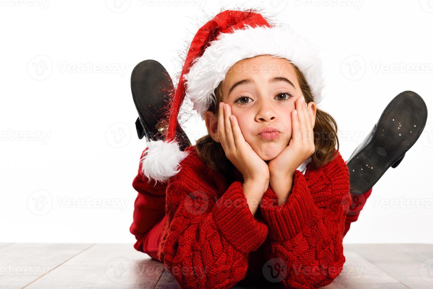 Adorable niña vistiendo gorro de Papá Noel tendido sobre un piso de madera foto