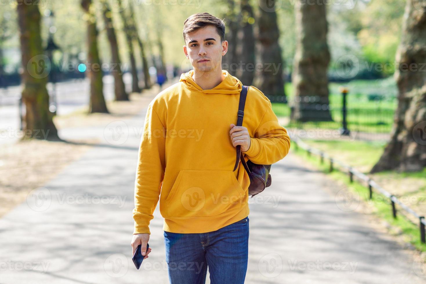 Young urban man using smartphone walking in street in an urban park in London. photo