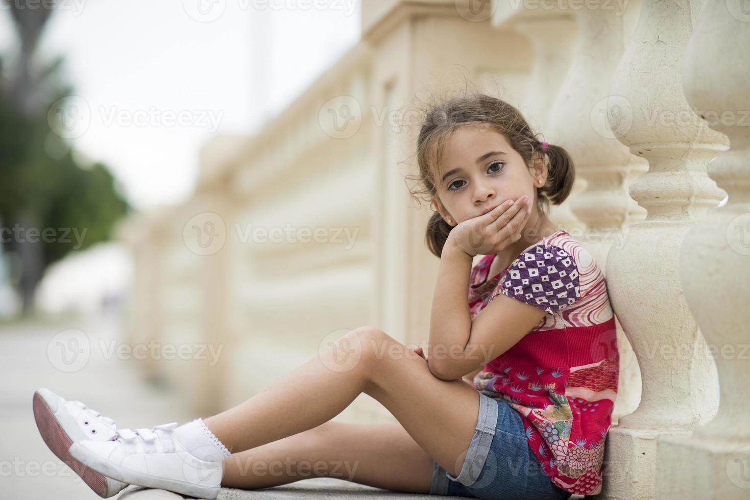 Adorable niña peinada con coletas sentada en el suelo foto