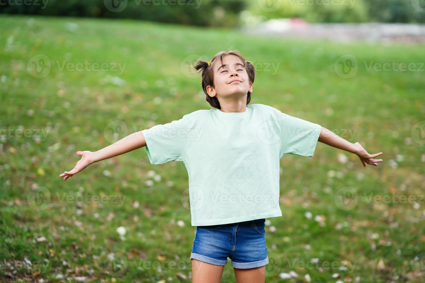 Niña de nueve años respirando con los brazos abiertos sobre la hierba foto