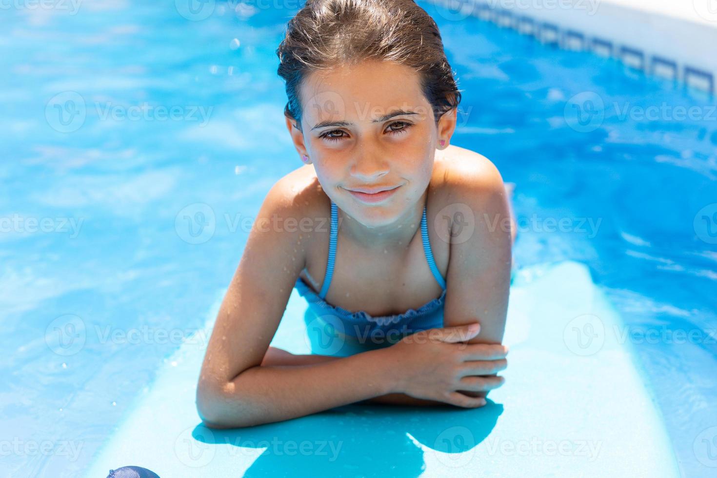 Cute girl playing with a bodyboard in a swimming pool. photo