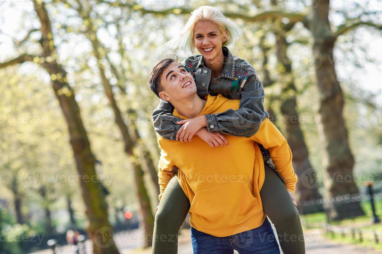 Funny couple in a urban park. Boyfriend carrying his girlfriend on piggyback. photo