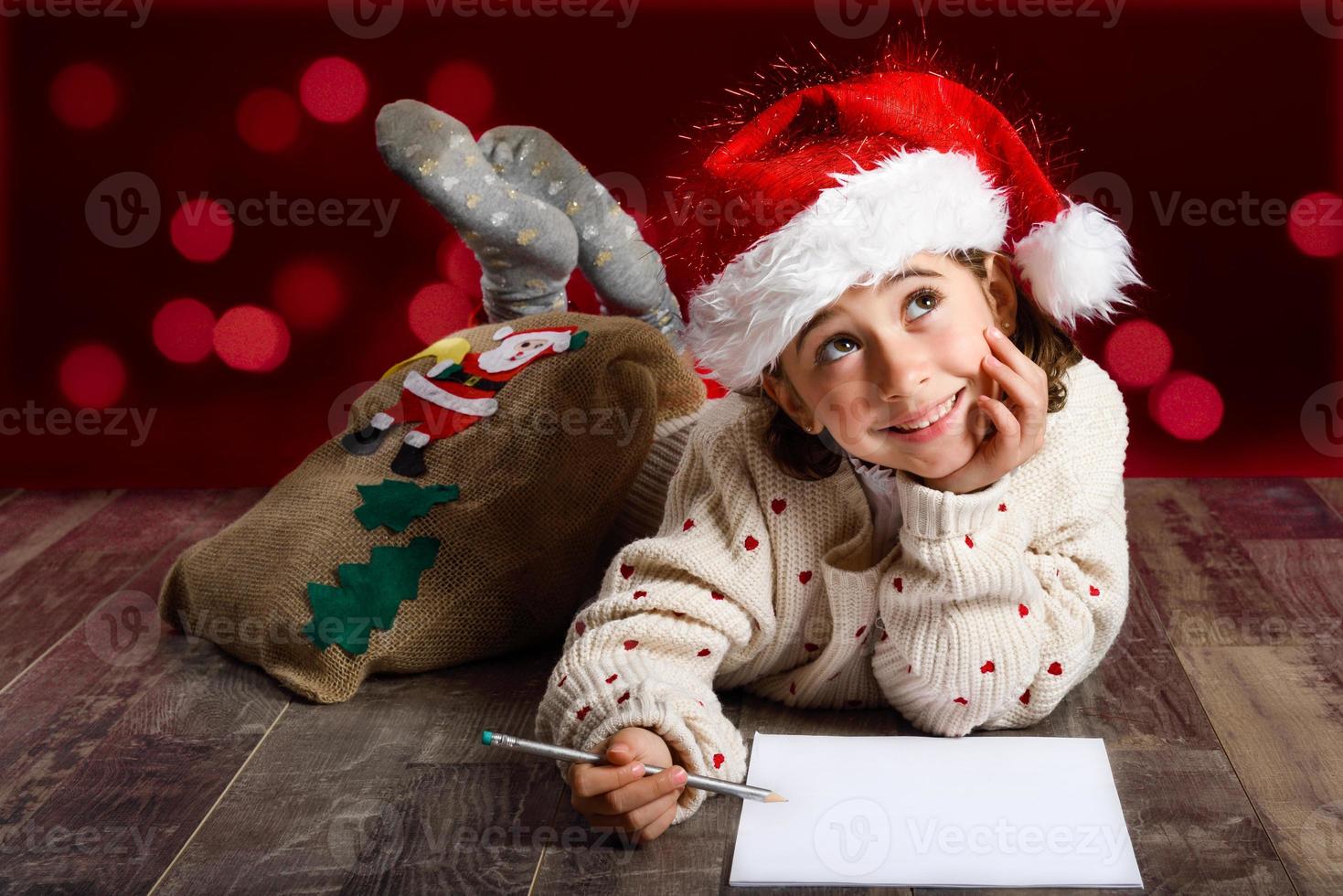 Adorable niña vistiendo gorro de Papá Noel escribiendo carta de santa foto
