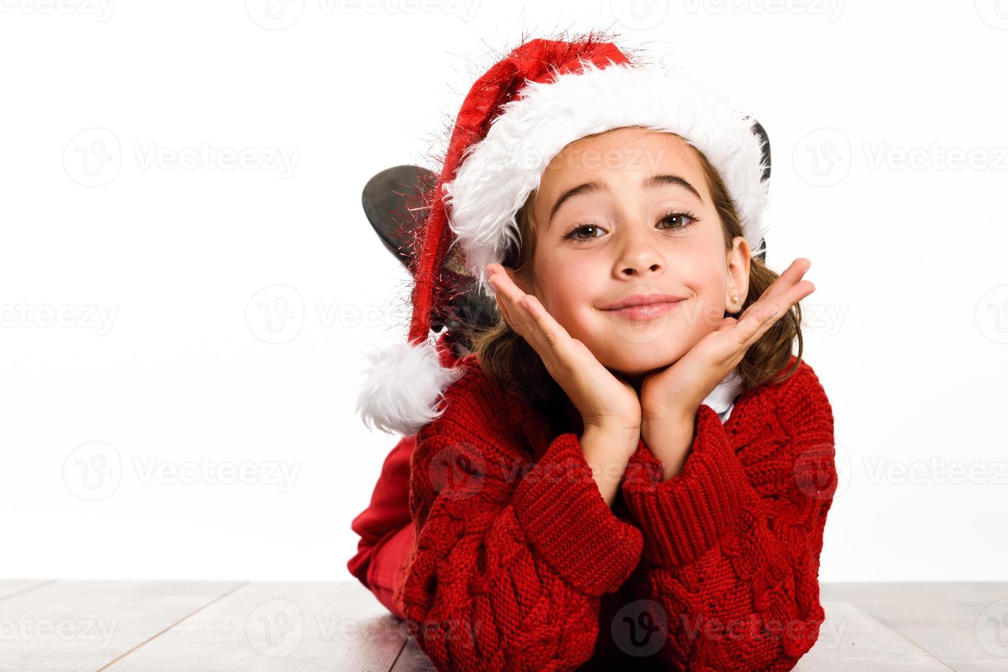 Adorable niña vistiendo gorro de Papá Noel tendido sobre un piso de madera foto