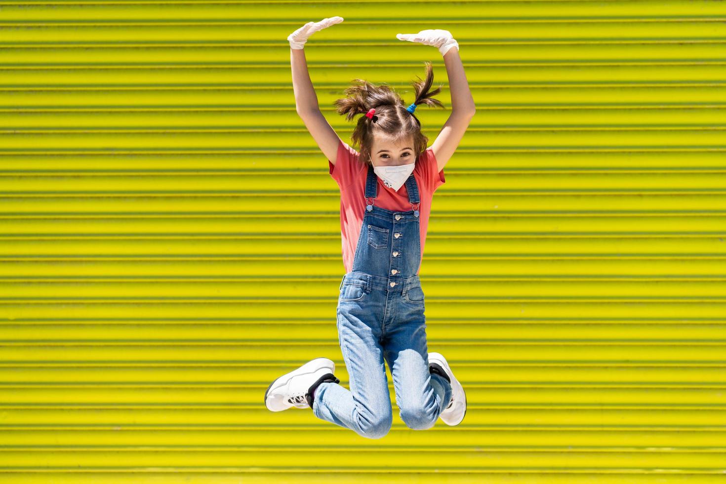 Child girl jumping wearing a protection mask against coronavirus photo