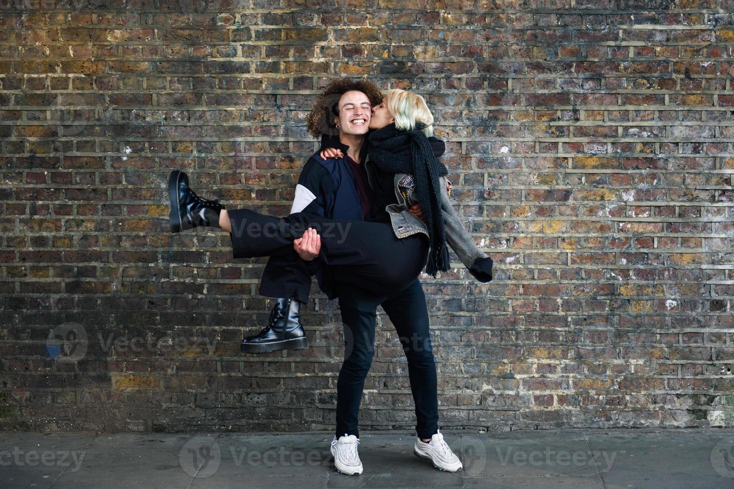 Man holding his girlfriend in his arms in front of a brick wall typical of London photo