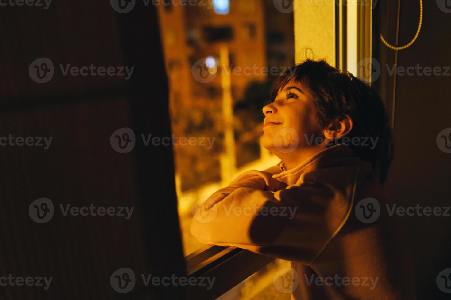 Girl looking out window at night to see the moon and stars. photo