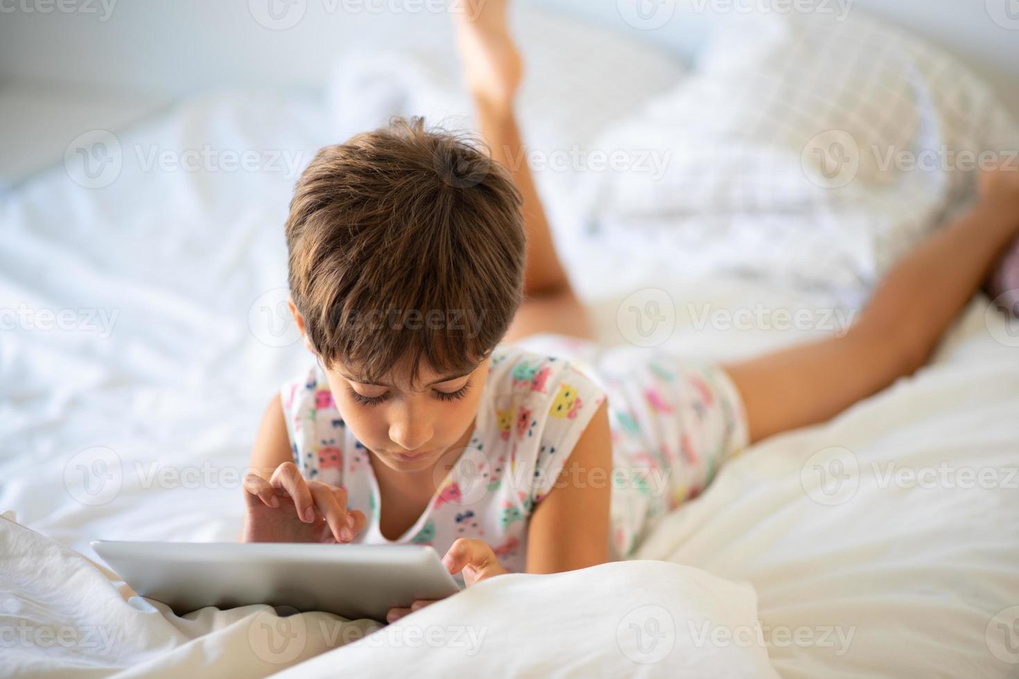Little girl playing with digital tablet on the bed. photo