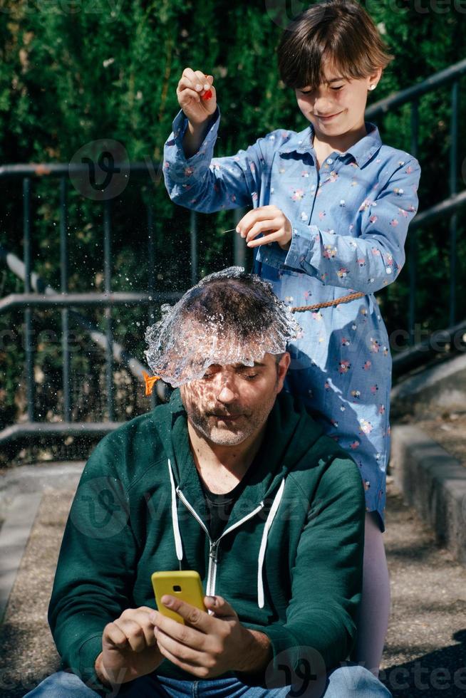 Girl blowing up a water-filled balloon over her father's head photo