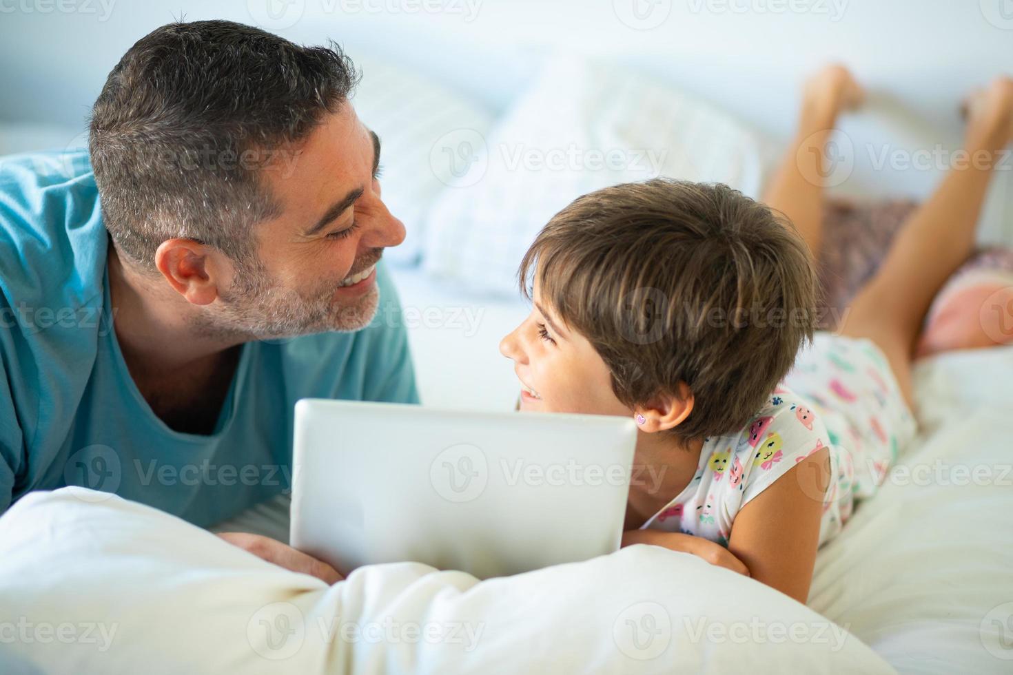 padre de mediana edad con su hija de ocho años con tableta digital en el dormitorio. foto