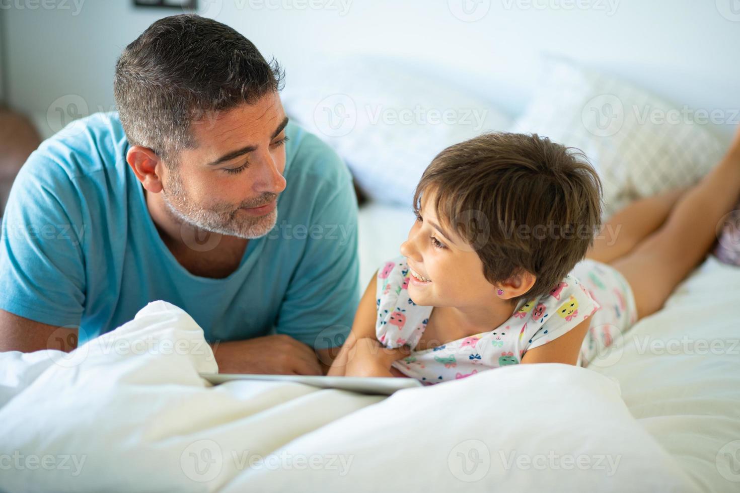 padre de mediana edad con su hija de ocho años con tableta digital en el dormitorio. foto